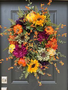 a wreath with flowers and pumpkins hanging on a front door, decorated with greenery