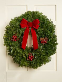 a christmas wreath with red bows and pine cones hanging on a white front door decorated for the holiday season