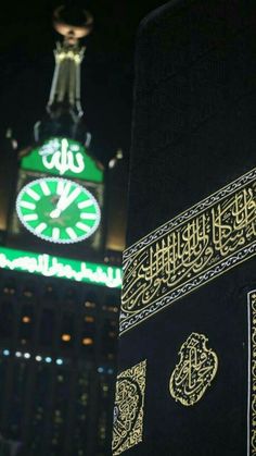 an illuminated clock tower in the middle of a city at night with arabic writing on it