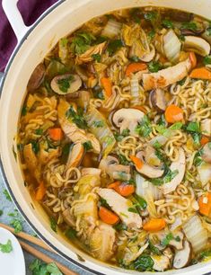 a pot filled with noodles and vegetables on top of a purple cloth next to chopsticks