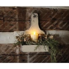 a lit candle sitting on top of a wooden shelf filled with flowers and greenery