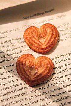 two heart shaped pastries sitting on top of an open book with pages in the background