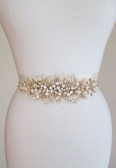 a bridal belt with pearls and beads is on display in front of a white mannequin