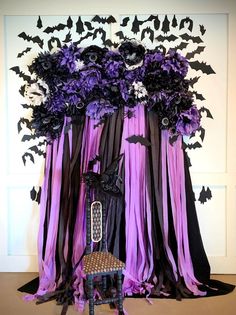 a chair sitting in front of a wall covered with purple and black ribbons, bats and flowers