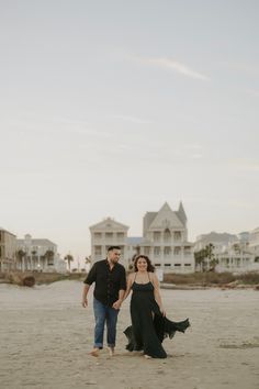 a man and woman walking on the beach with houses in the backgrouds