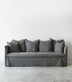 a gray couch sitting on top of a cement floor next to a white wall with lots of pillows