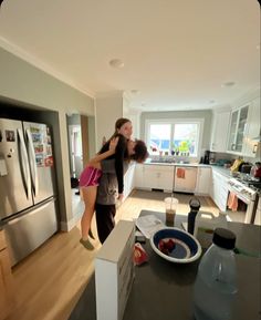 two women hug in the middle of a kitchen with stainless steel refrigerator and dishwasher