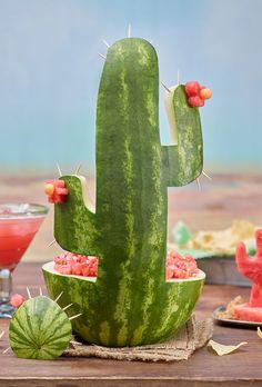 a watermelon cactus sitting on top of a wooden table next to two cocktail glasses