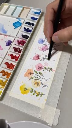 someone is painting flowers with watercolors on paper