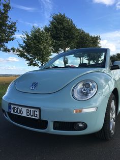 a light blue volkswagen beetle cab parked on the side of the road in front of a tree