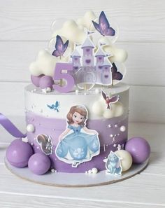 a purple and white birthday cake with princess figures on the top, surrounded by decorations