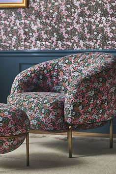 an upholstered chair and footstool in front of a floral wallpaper