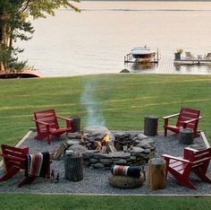 a fire pit with chairs around it in the middle of a grassy area next to water