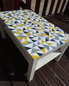 a white table with yellow and grey triangles painted on the top, sitting on a wooden deck