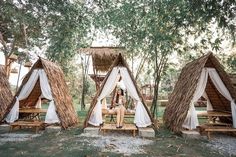 a woman sitting on a wooden bench in front of some huts with white drapes