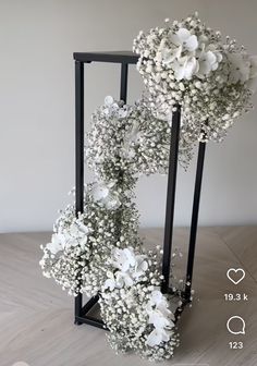 two black stands with white flowers in them on a wooden floor next to a wall