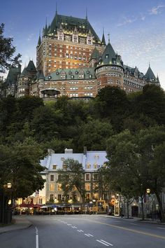 a large building sitting on top of a lush green hillside next to trees and buildings