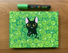 a green notebook with a black cat on it next to a marker and some crayons