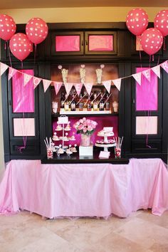 a pink and black dessert table with lots of balloons on the wall behind it,