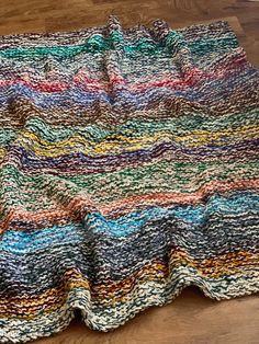 a multicolored crocheted blanket is laying on the floor