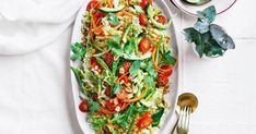 a white plate topped with salad next to a bowl of dressing and spoons on a table