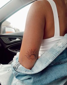 a woman with a sun tattoo on her left arm sitting in a car and looking out the window