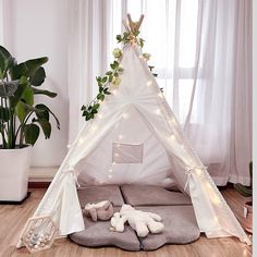 a teepee tent with lights and stuffed animals on the floor in front of it