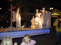 some people are standing in front of an outdoor stage decorated with white cloths and lights