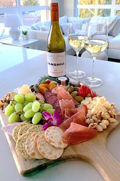 a wine bottle and some grapes on a table with a platter of cheeses and crackers