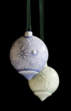 two glass ornaments hanging from a green ribbon on a black background with snowflakes