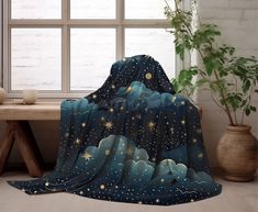 a blanket with stars and clouds in the night sky on a table next to a potted plant