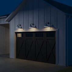 three lights on the side of a garage door in front of a barn at night