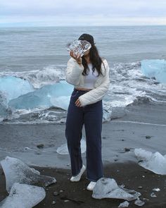 a woman standing on top of a beach next to icebergs and looking at her cell phone