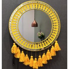 a round mirror with tassels hanging from it's sides and a vase on the other side