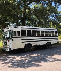 an old school bus is parked on the side of the road in front of some trees