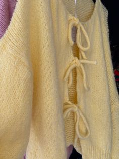 a yellow sweater with laces hanging on a hanger next to other knitted clothing