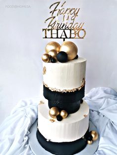 a three tiered white and black cake with gold decorations on it's top