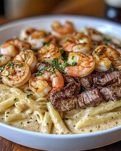 a white bowl filled with pasta and shrimp on top of a wooden table next to a fork