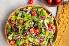 a salad in a wooden bowl with tomatoes and other vegetables on the table next to it