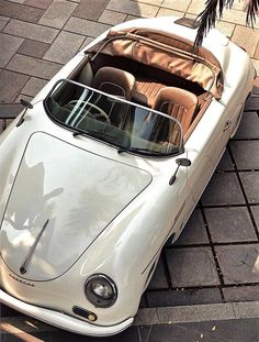 an old white sports car parked on the side of the road next to a palm tree