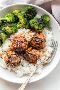 meatballs and broccoli are served over white rice in a bowl with a fork