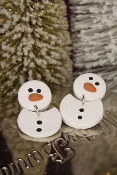 two white snowmen sitting next to a christmas tree