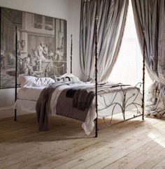 a bed sitting in a bedroom next to a window with drapes on the sides