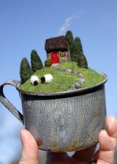 someone is holding up a cup with a house on it and trees in the background