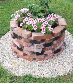 a brick planter filled with pink and white flowers on top of graveled ground