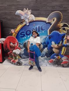 a woman standing in front of a sonic the hedgehog sign with other characters behind her