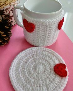 two crocheted coasters with red hearts on them sitting next to a coffee cup