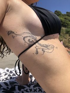 a woman with a tattoo on her lower back and arm is sitting on the beach