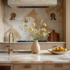 a bowl of lemons sits on the kitchen counter next to a vase with flowers in it