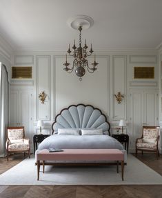 a bedroom with a large bed, chandelier and two chairs in front of it